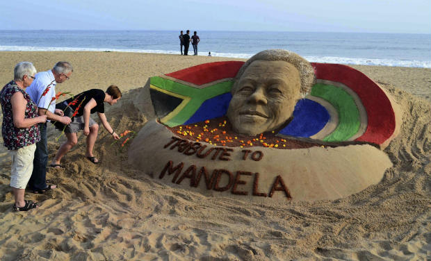 Tourists offer floral tributes near a sand sculpture of Nelson Mandela on a beach in Puri, Odisha on Friday - AP Tourists offer floral tributes near a sand sculpture of Nelson Mandela on a beach in Puri, Odisha on Friday - AP